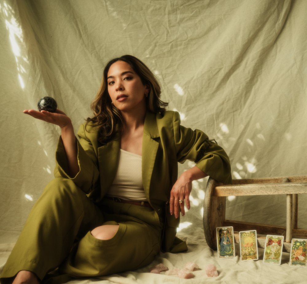 Charlene Platon seated with tarot cards and rose quartz, holding a dark crystal sphere