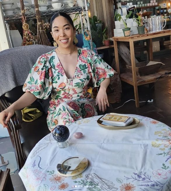 Charlene in a floral dress at her reading table with a crystal ball and tarot deck