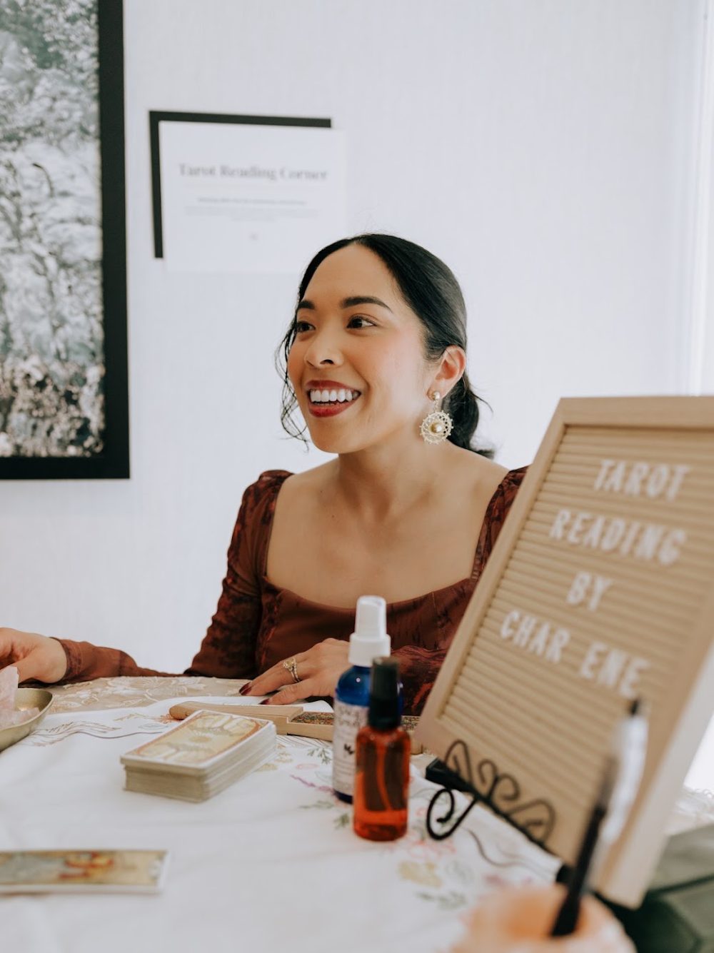 Charlene smiling at a tarot reading corner with a letterboard sign reading Tarot Reading by Charlene