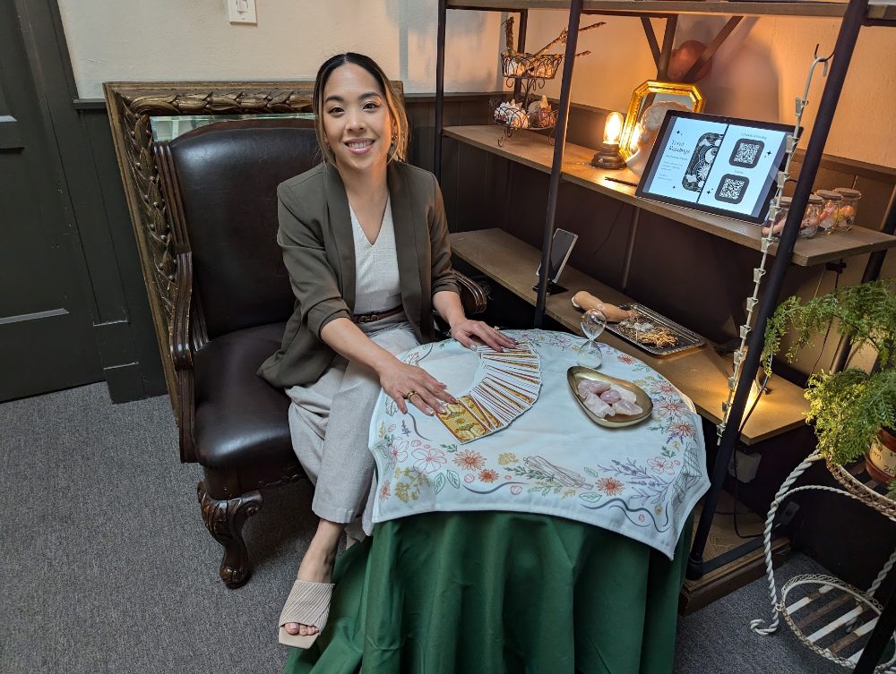 Charlene seated at her reading table with fanned tarot cards, rose quartz, and a booking screen