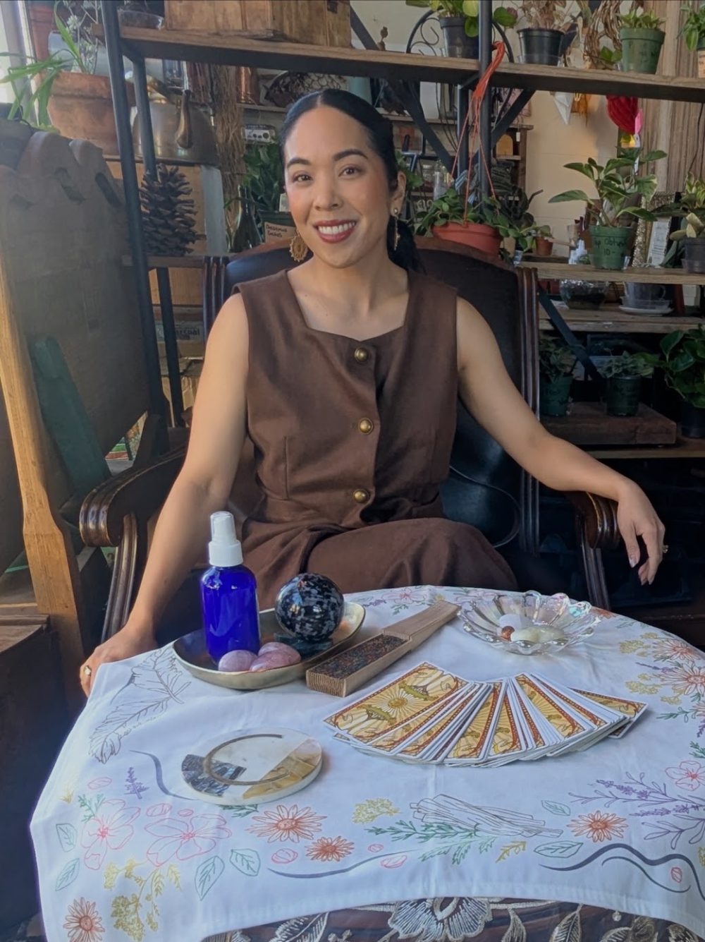 Charlene at a plant-filled shop behind her tarot table with cards fanned out